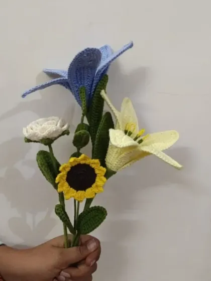 A cool-toned crochet bouquet with blue and yellow lilies, a white rose, and a sunflower. The color possibilities are endless with our handmade flowers.