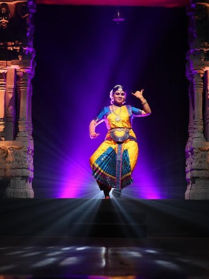 A student stands poised for her debut performance. The striking lighting and stage design are all part of creating a memorable Arangetram, a celebration of years of hard work and dedication to the art form.