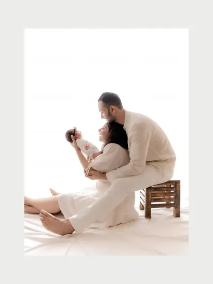 In this color portrait, the soft lighting and gentle poses create a serene and loving scene. New parents hold their baby, their connection evident in their posture and gaze, capturing the quiet joy of the newborn phase.