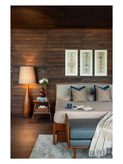 A closer view of the bedroom, highlighting the mix of textures from the wooden walls, soft rug, and upholstered bench. The lighting is layered to create a relaxing and intimate mood.
