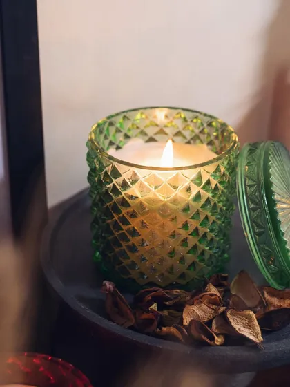 A close-up of our green diamond-cut jar candle, filled with our limited-edition Peach Bellini scented soy wax. The lid is off, and the flame casts a warm, inviting glow.