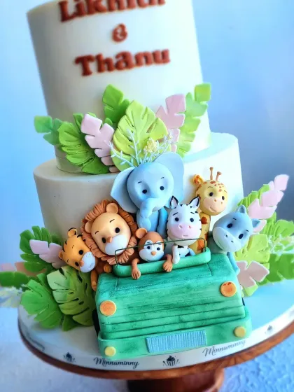 A two-tiered safari cake perfect for a wedding or engagement. The design features a jeep full of cute, hand-sculpted fondant animals peeking out from behind tropical leaves.
