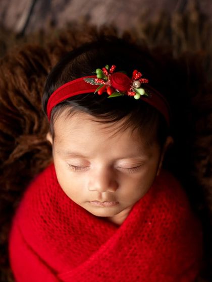 Another angle focusing on the baby's serene expression. The deep red wrap and headband create a striking and beautiful color combination for this newborn girl.