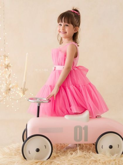 A confident and happy portrait of a little girl in a pink dress, posing with her matching pink toy car.