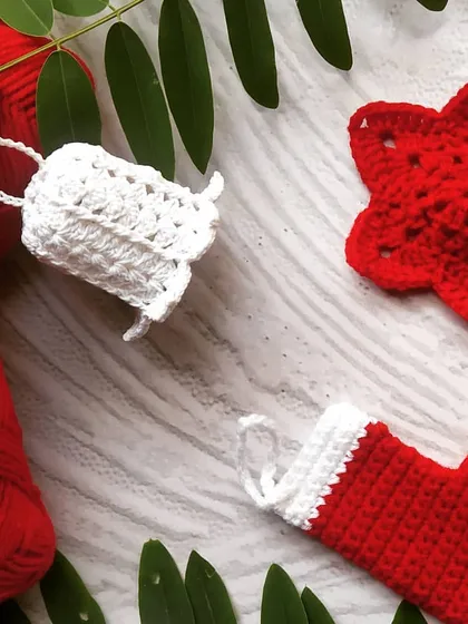 A close-up of our classic Christmas crochet ornaments. This set includes a white bell, a red star, and a miniature red and white stocking, perfect for a traditional holiday theme.