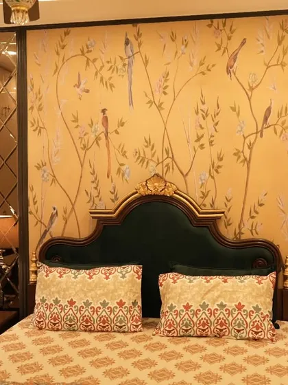 A vintage-inspired bedroom with a classic appeal. The design features a dark green velvet headboard, chinoiserie-style wallpaper, and elegant diamond-patterned mirror panels on either side of the bed.