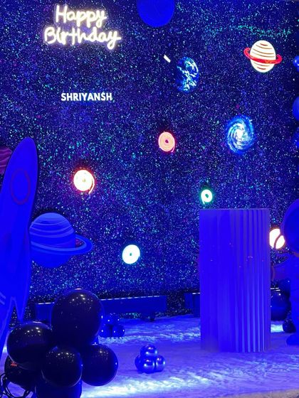 A wider view of the space party setup, showing the rocket ship prop, the planet-filled backdrop, and the dark, chrome balloons that complete the galactic atmosphere.