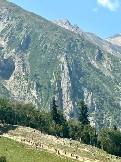 A wide view of the lush green valleys and the trail winding through them. The sheer size and beauty of the Himalayan landscape is breathtaking.