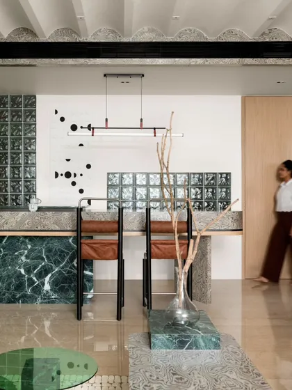 The breakfast counter, with its green marble base and textured veneer top, is a visual focal point. The custom wall art and glass block backdrop add layers of interest, turning a functional area into a design statement.
