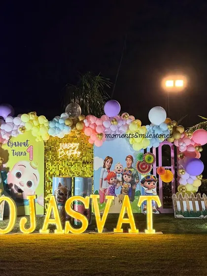 An outdoor Cocomelon party for Ojasvat. This wide shot shows the full scale of the setup against the evening sky, with the lights making the decor pop.