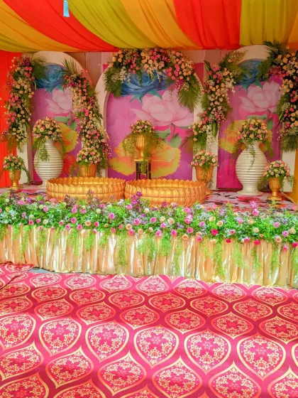 A full view of a Haldi decoration setup, showing the stage with floral arrangements, traditional urlis, and a colorful fabric canopy.