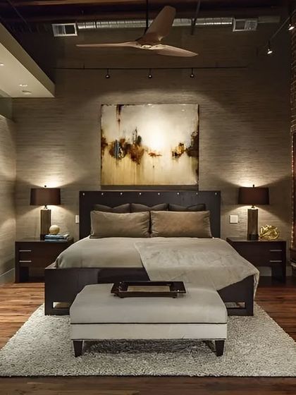 An industrial-style bedroom with an exposed brick wall and warm wood flooring. The design combines rustic elements with modern comforts, including a sliding barn door and soft, ambient lighting.