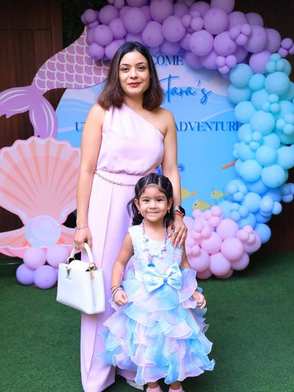 A mother and daughter pose in front of the "Under the Sea Adventure" backdrop. The pastel colors of the decor and their outfits create a lovely, coordinated photo.