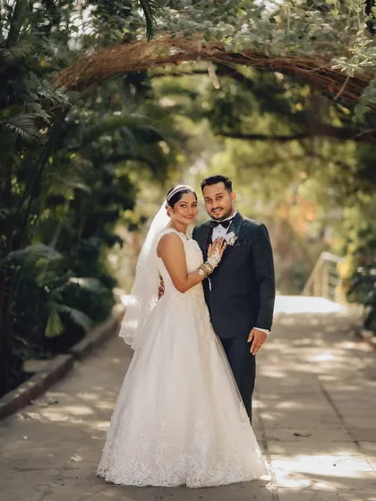 A full-length portrait of the couple under a natural archway of trees. This image showcases their wedding attire and the beautiful scenery of their chosen venue.