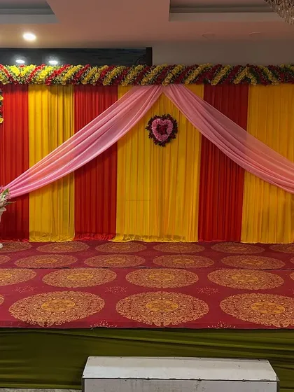 A simple stage backdrop with red and yellow drapes and a small floral heart, suitable for small functions or as a photo wall.
