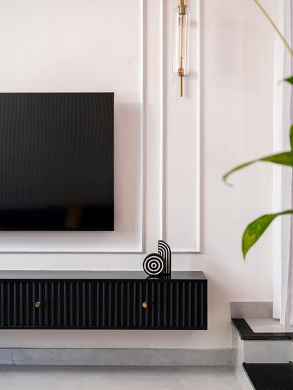 A close-up of the sleek black TV unit, showing the fluted texture and the small, elegant gold-knob handles.