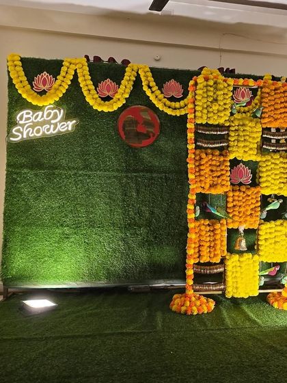 A traditional marigold and lotus themed baby shower backdrop with a neon sign, before the seating is placed.