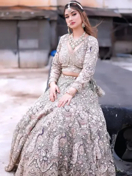 A sitting pose in the sage green lehenga, showing the beautiful flare and intricate details of the skirt.