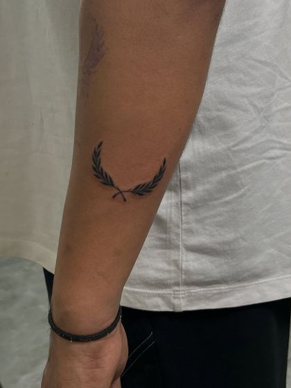 A simple and elegant laurel leaf tattoo on the forearm. This minimalist design is a classic symbol of victory and honor, created with delicate, clean lines.
