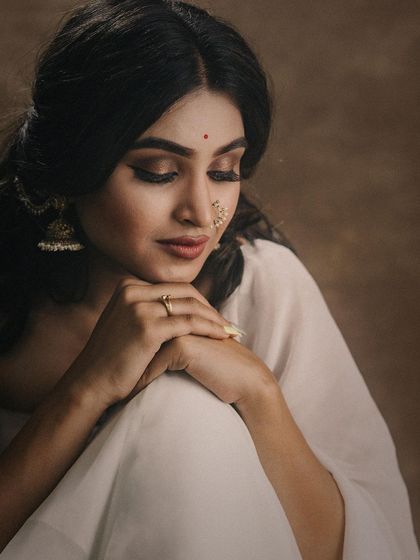 A serene and classic portrait of a model in a simple white saree. Her contemplative expression and the earthy, textured backdrop create a timeless, painterly effect.