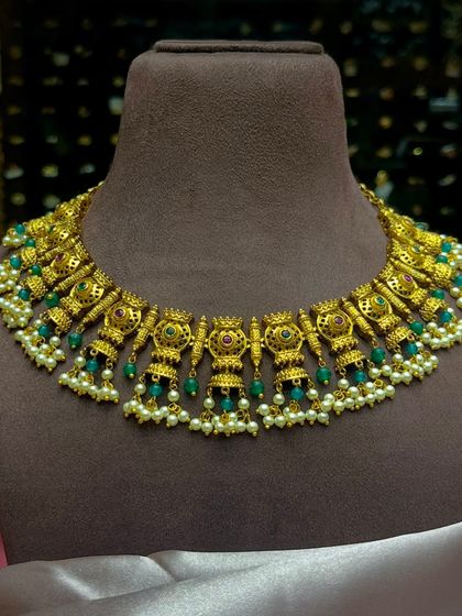 A beautiful temple jewellery choker necklace with intricate carvings and pearl and green bead drops. This piece adds a touch of divine elegance to any traditional outfit.