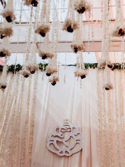 The decor of a daytime Odia wedding, featuring a Ganesha motif against a backdrop of white curtains and hanging floral arrangements. These details set the serene and sacred tone for the ceremony.