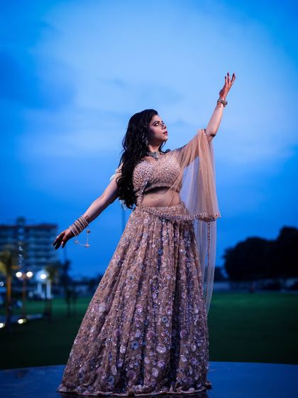 A woman in a beautiful lehenga poses against a twilight sky, creating a dramatic and elegant silhouette.