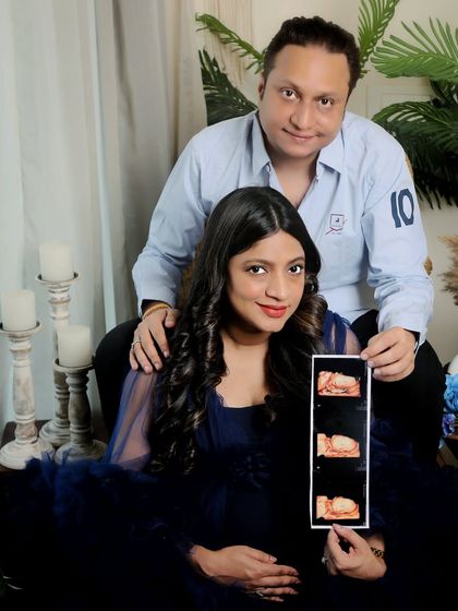 A beautifully composed announcement photo. The mom-to-be, in an elegant blue gown, holds up the sonogram while her partner looks on, framed by our boho studio decor.