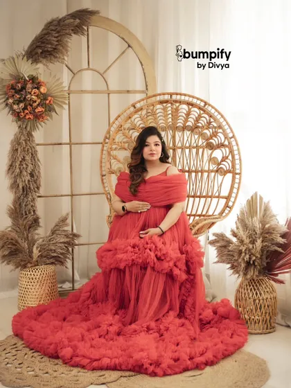 A bold and beautiful statement in red. The mom-to-be looks like royalty in this vibrant red ruffled gown, seated on a wicker peacock chair in a boho-themed setup.