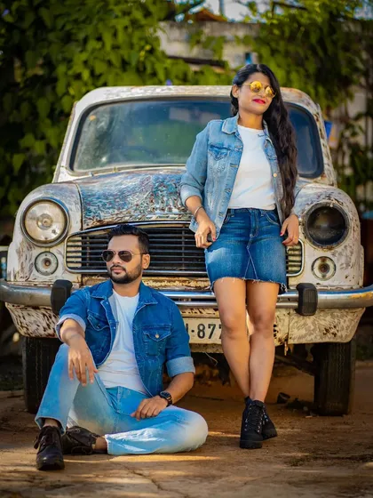 A full-body shot of a couple in stylish denim outfits posing with a vintage car, capturing a cool and confident vibe.