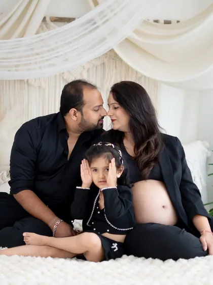 A sweet and funny family moment. The soon-to-be big sister covers her eyes playfully while her parents share a loving moment, creating a candid and memorable family portrait.