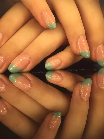 A simple yet stylish French manicure with light green tips on beautifully shaped almond nails.