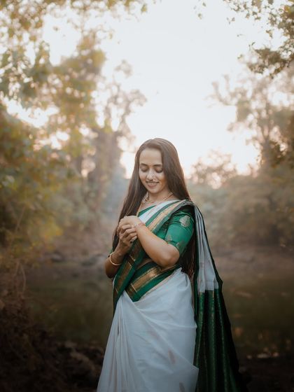 A beautiful full-length portrait of a bride in a traditional white and green saree for her Haldi ceremony, set in a tranquil forest.