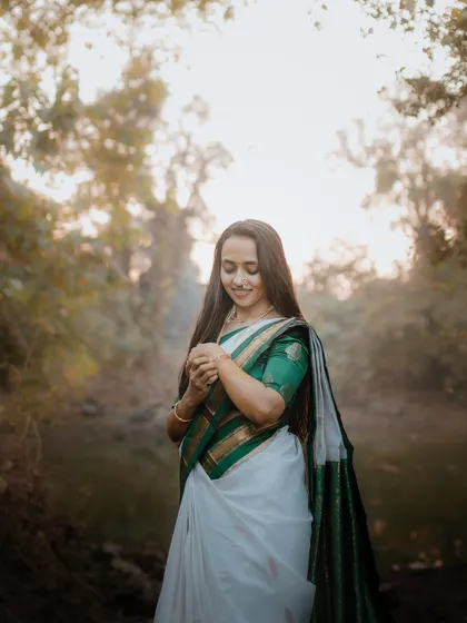 A beautiful full-length portrait of a bride in a traditional white and green saree for her Haldi ceremony, set in a tranquil forest.