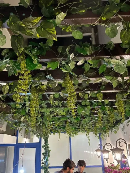 A beautiful overhead installation using artificial vines on a wooden pergola. This creates a lush canopy effect for a cafe's seating area, providing a feeling of being in a garden.