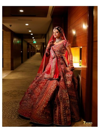 A stunning portrait of the bride in her red lehenga, captured in a corridor. The lighting highlights the rich colors and intricate details of her outfit and makeup.
