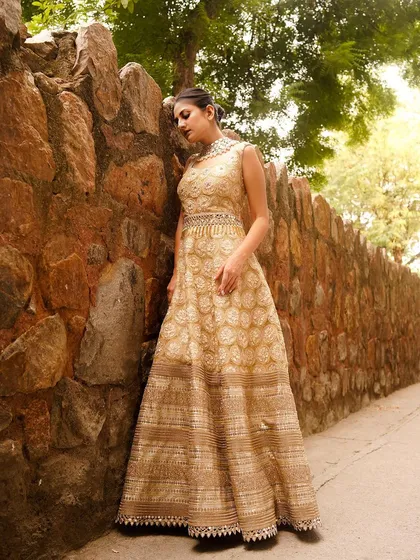 An outdoor shot of a model in a golden gown against a rustic stone wall. The natural light beautifully illuminates the intricate patterns of the dress, creating a timeless and elegant portrait.