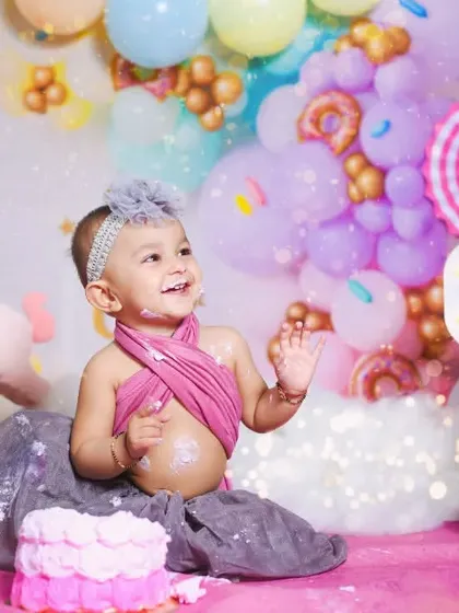 A sweet celebration in a custom Candyland setup. This little girl is enjoying her first birthday cake surrounded by pastel balloons, donuts, and a unicorn friend.