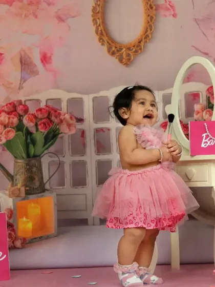This little Barbie fan laughs with joy, playing with lipstick at a vanity in a room filled with pink decor and shopping bags.