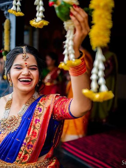 A candid shot of a bride laughing while interacting with traditional floral garlands. Her genuine joy is the focus of the image.