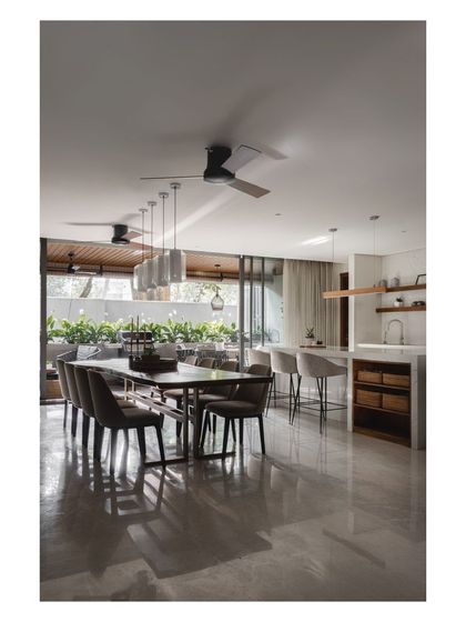 This wide shot captures the entire open-plan area, from the kitchen island to the eight-seater dining table and the outdoor deck beyond. The polished floor reflects the light beautifully.