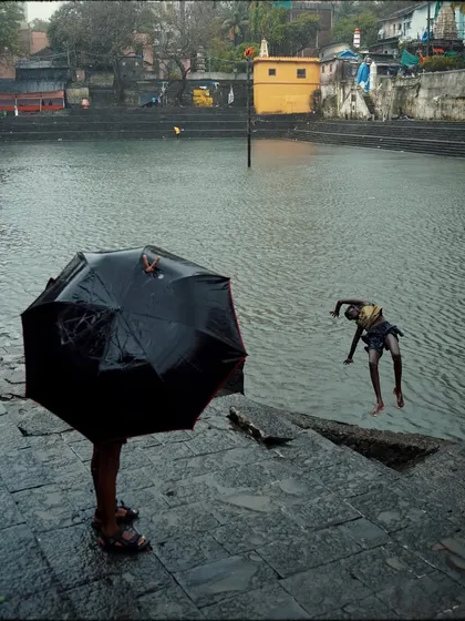 A playful and dynamic composition at Banganga, with one person hidden under an umbrella in the foreground while another dives into the water behind them. It tells a story of different ways to enjoy the rain.