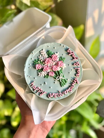 The floral anniversary bento cake, held in hand to show its cute, personal size. Perfect for a sweet, intimate celebration.