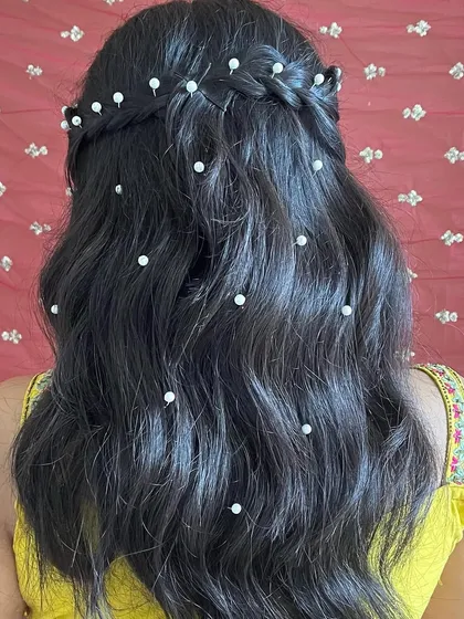 A beautiful hairstyle for a daytime event. This half-up braided look is adorned with delicate pearls, adding a touch of elegance to her beachy waves.