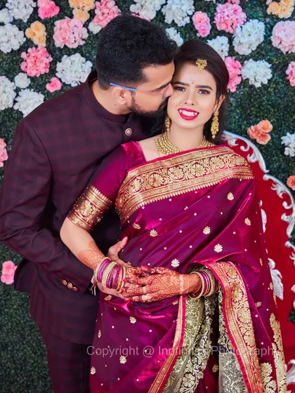 A lovely portrait of a couple in traditional attire against a floral wall. The groom's affectionate gesture adds a layer of warmth and intimacy to the shot.