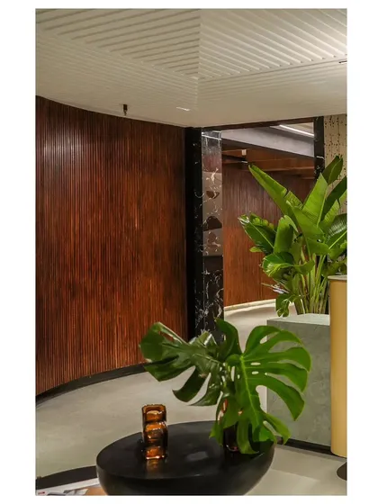 The fluid wood wall is not just a visual element; it also integrates functional features like this reading nook, where the wall curves to create a backdrop for a small seating area.