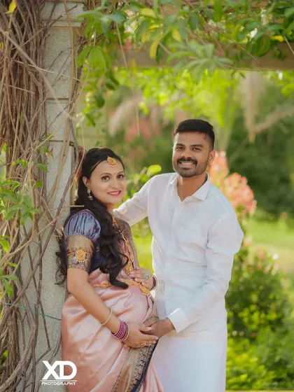 A smiling couple posing under a vine-covered archway, dressed in elegant traditional wear.