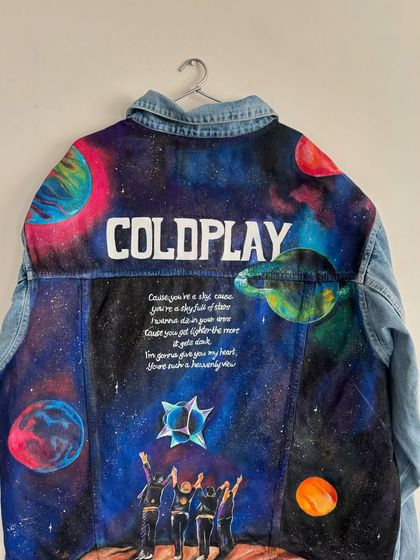 The full view of the completed light-wash denim jacket, hung up to display the entire cosmic scene. This perspective shows how all the elements, from the planets to the band members, are balanced in the composition.