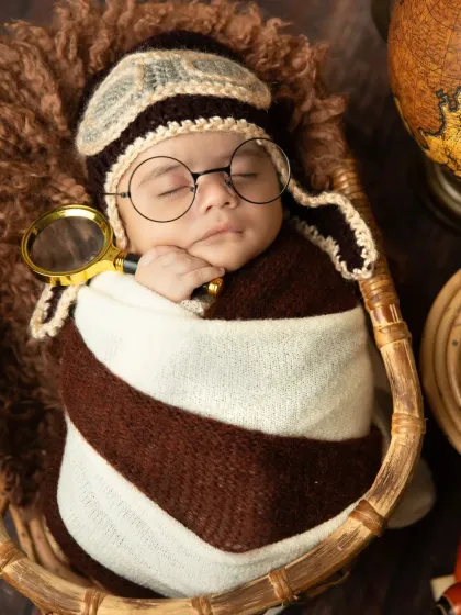 Another adorable shot of the sleeping explorer, holding a magnifying glass. The knitted aviator cap completes this charming themed look.