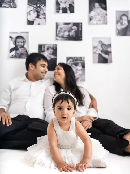 A unique family portrait with the baby girl front and center. The wall of memories behind them tells the story of their first year together.